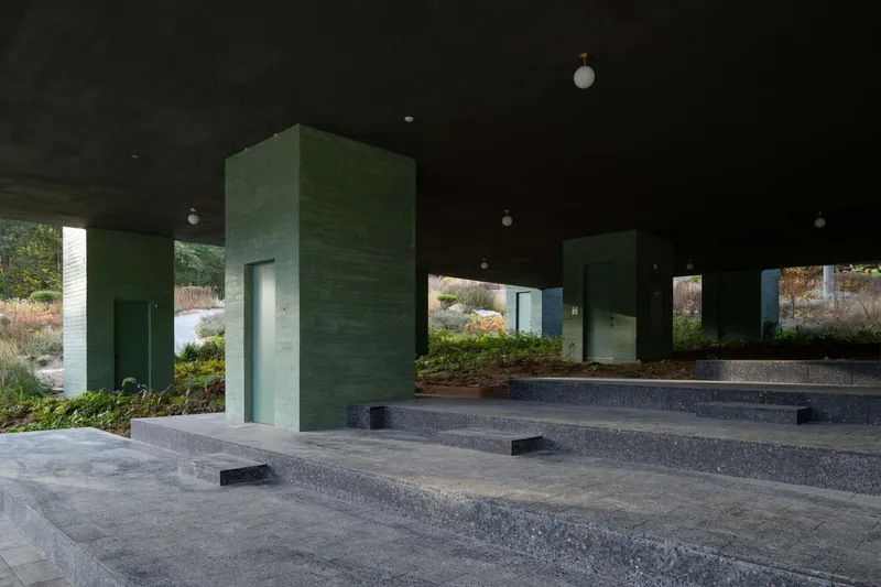 Stepped terrazzo platforms with green concrete service towers beneath the elevated building volume