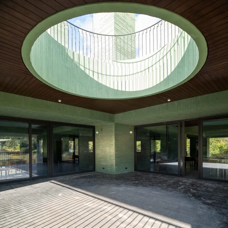 Circular skylight with vertical louvers above a timber-clad ceiling in a semi-outdoor space