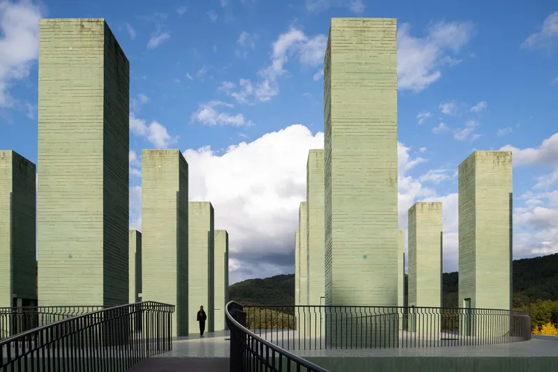 Green concrete towers rising from a curved terrace with metal railings under a partly cloudy sky
