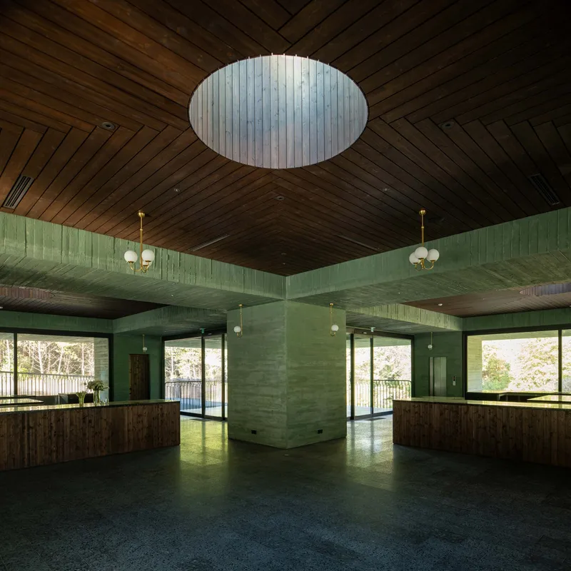 Interior hall with oval skylight, timber ceiling panels and green board-formed concrete columns