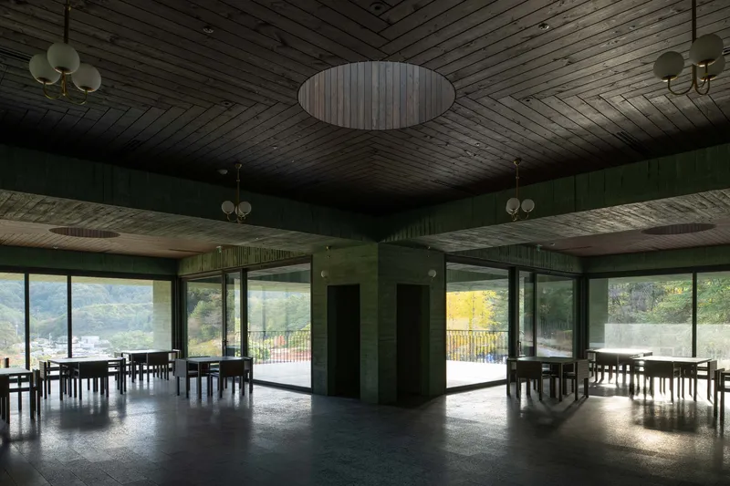 Interior hall with exposed timber ceiling, green columns, and floor-to-ceiling windows overlooking mountains