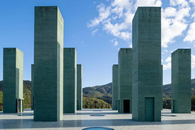 Grid of varied-height concrete towers framing distant hills under blue sky with clouds