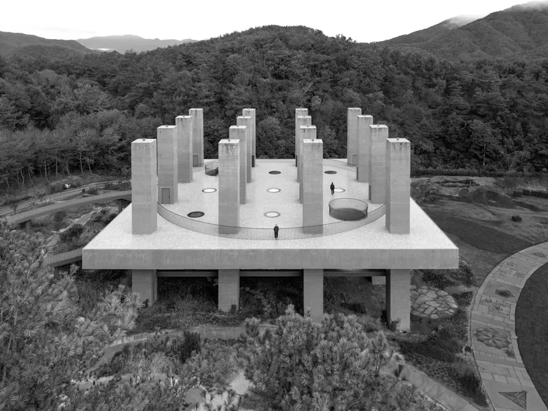 Aerial view of concrete roof with circular openings and tower groupings against forested mountains