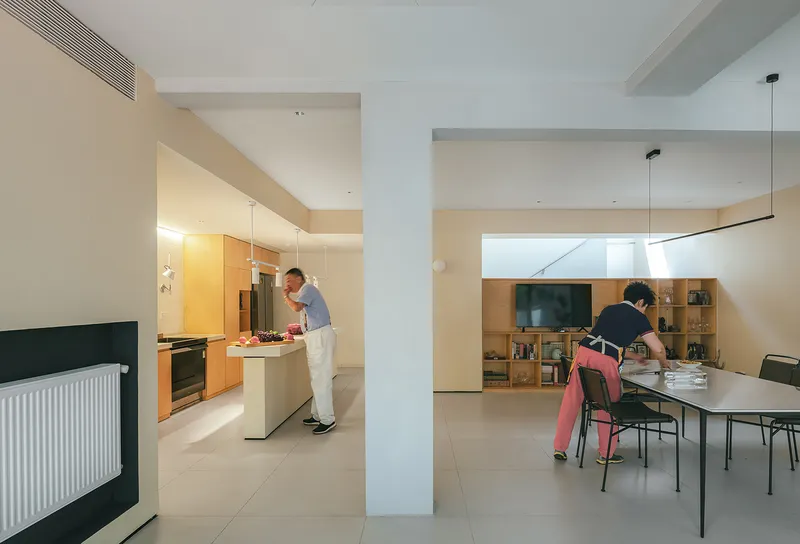 Open-plan kitchen and dining area separated by white columns with two people preparing food