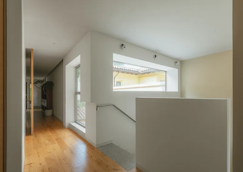 Upper-level hallway with wood flooring and horizontal window overlooking neighboring rooftops