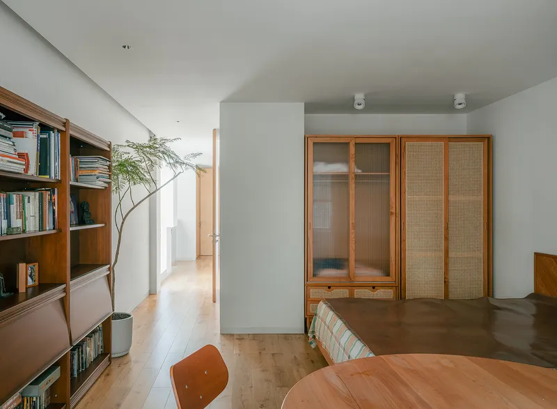 Living area with curved timber bookshelf and rattan-panelled wardrobes under soft natural light