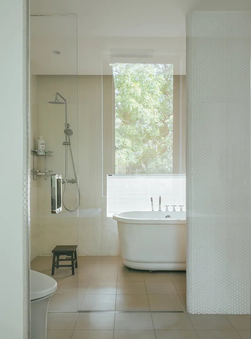 Bathroom with freestanding tub and glass shower enclosure beside a window overlooking green foliage
