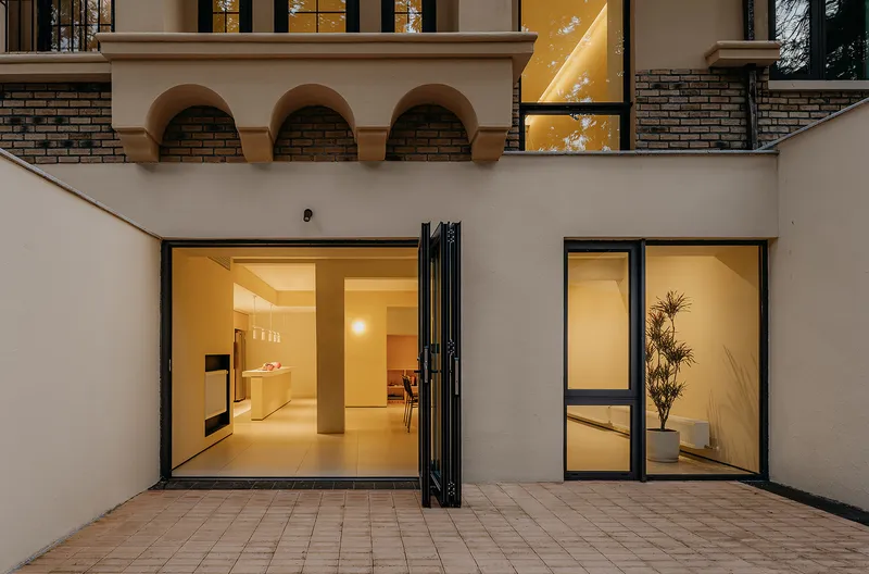 Courtyard at dusk with brick paver floor and black-framed glazed openings illuminated from within