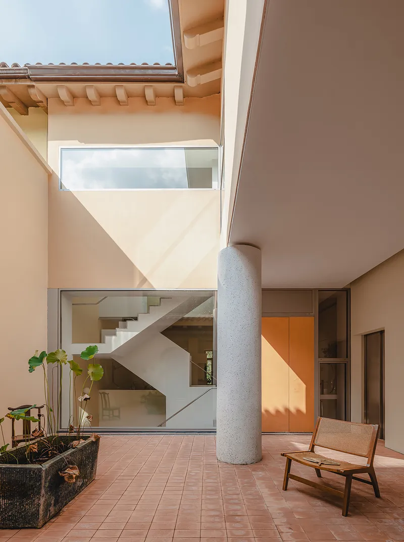 Terracotta tile courtyard with cylindrical concrete column and view to interior staircase above