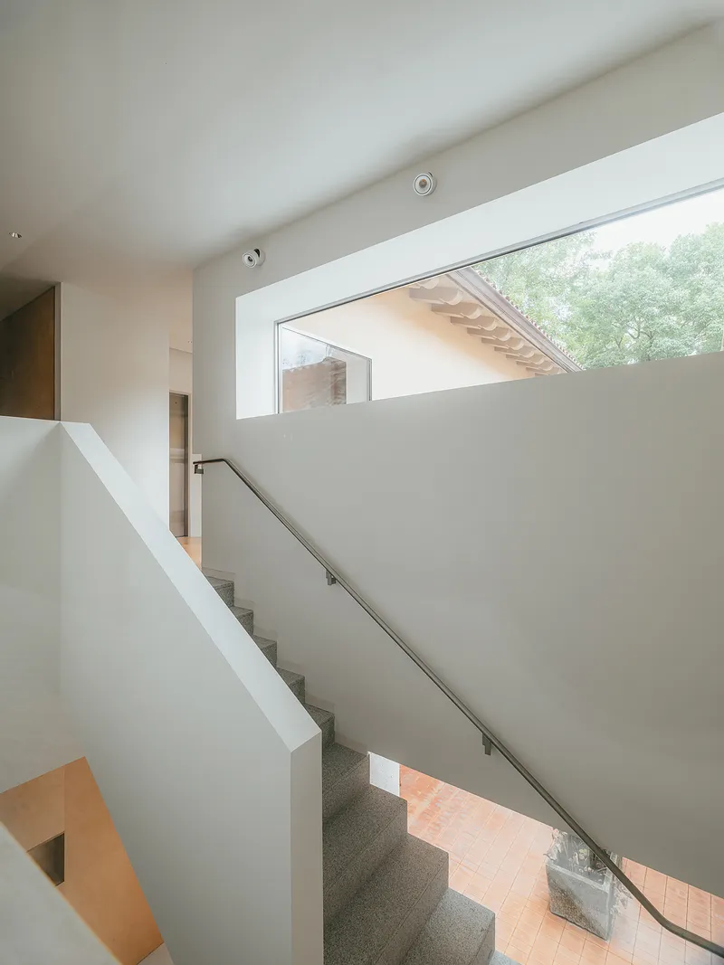 Upper level staircase with terrazzo treads and metal handrail beneath a clerestory window