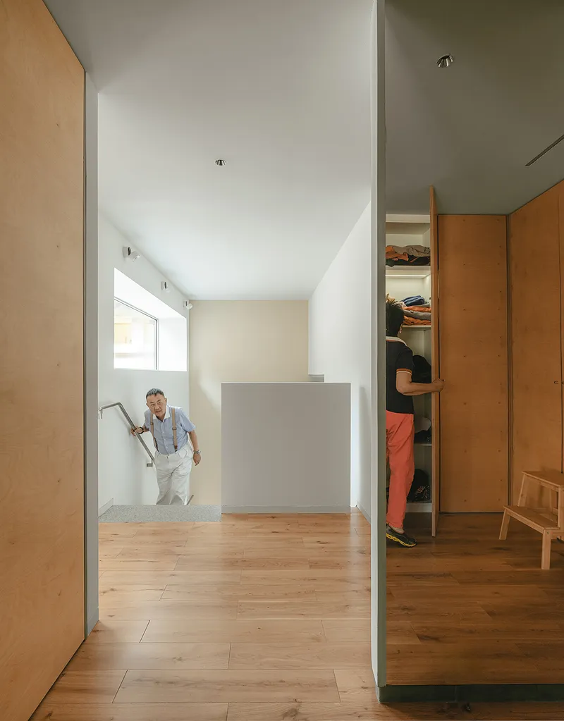 Timber-lined hallway with person descending stairs toward an open wardrobe niche