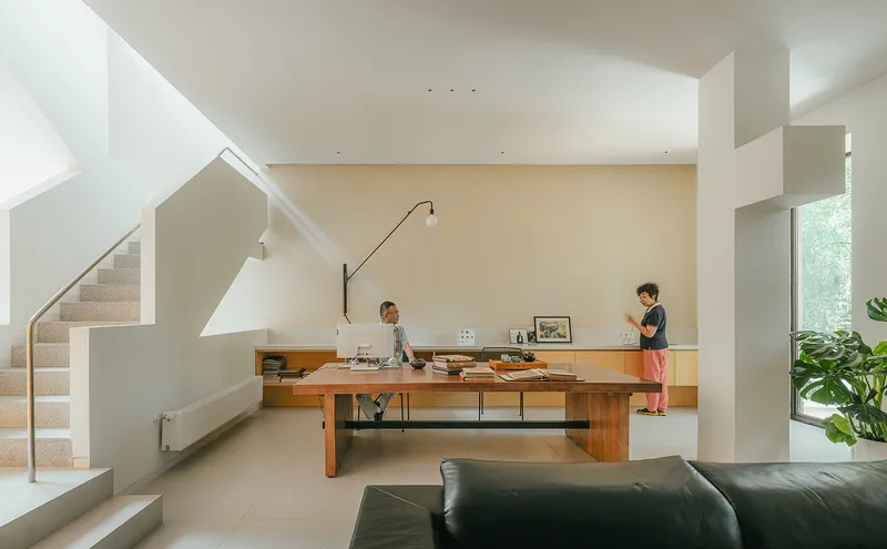 Double-height living area with timber dining table and two occupants beneath natural light