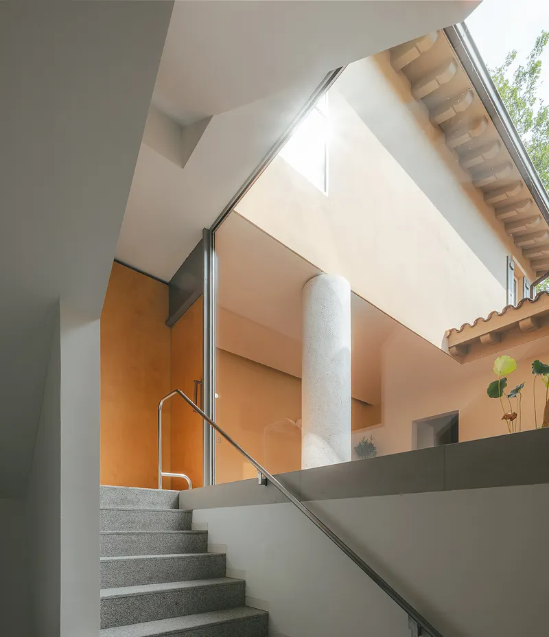 Terrazzo staircase with stainless steel handrail rising toward a light-filled upper level