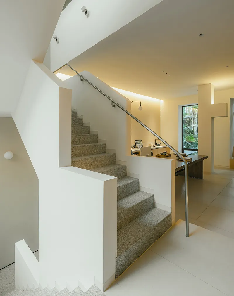 Double-height stairwell with terrazzo treads and indirect lighting along the ceiling edges