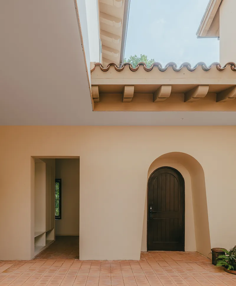 Courtyard with ochre stucco walls, arched door, terracotta tile floor and exposed timber eaves