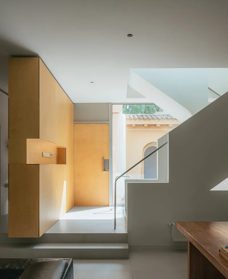 Entry hall with plywood storage wall and view through to courtyard with tile roof
