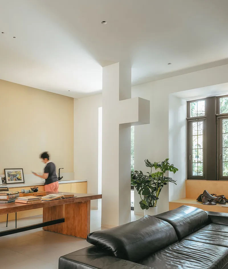 Living room with white geometric partition and a person moving past a wooden desk in afternoon light