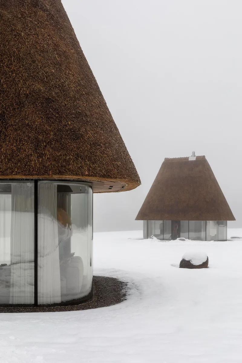 Two conical thatched volumes standing in a snow-covered field in misty conditions
