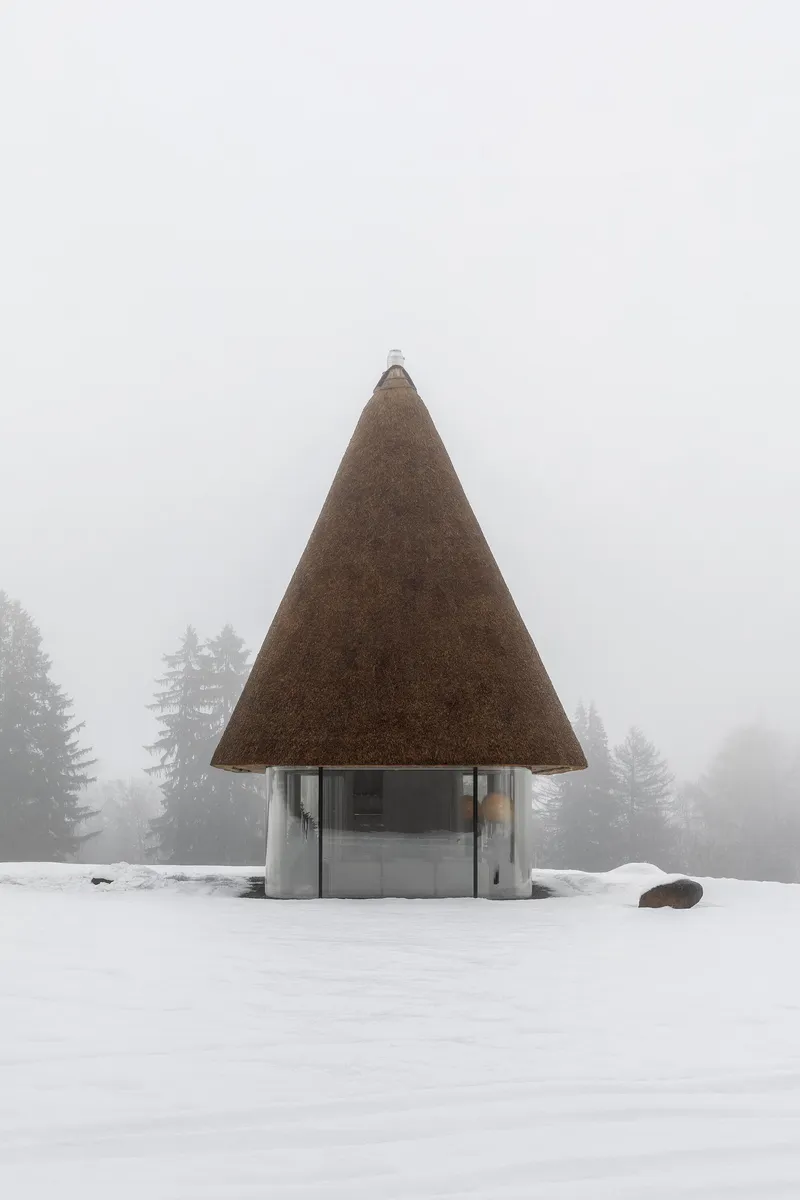 Front elevation of the conical thatched pavilion surrounded by fog and evergreen trees