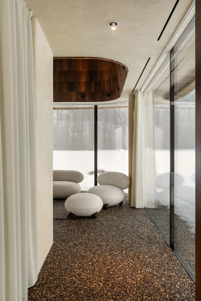 Interior view of exposed aggregate floor with white cushions and woven timber ceiling pendant near curtained wall
