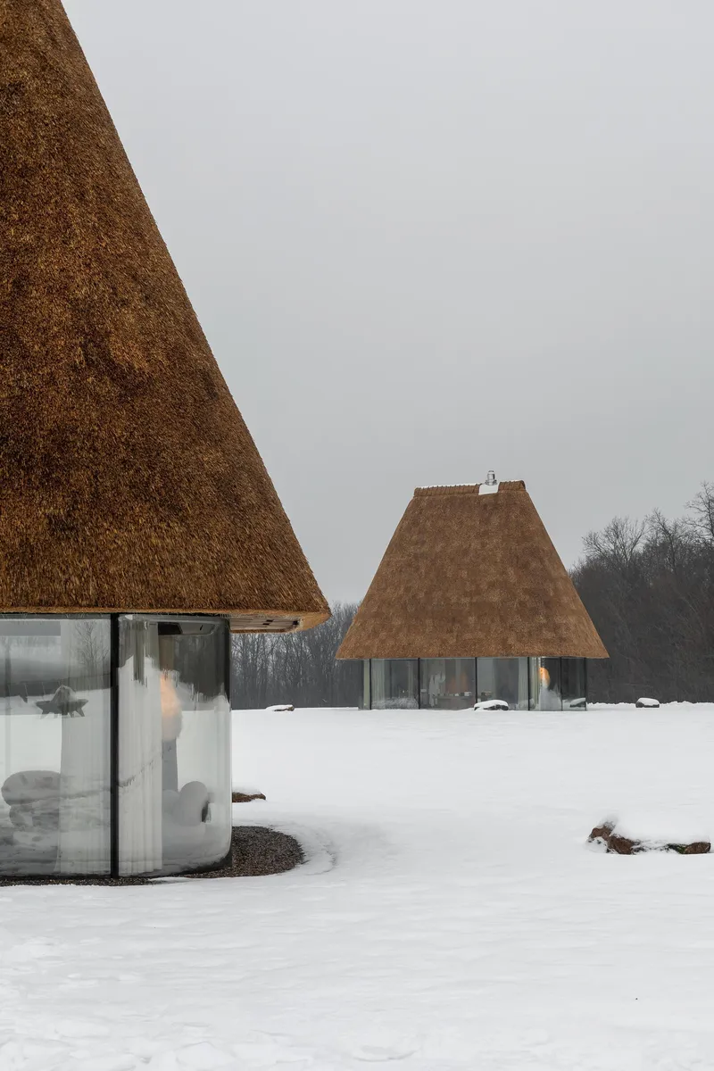 Two thatched roof pavilions on a snowy field with bare trees visible along the horizon