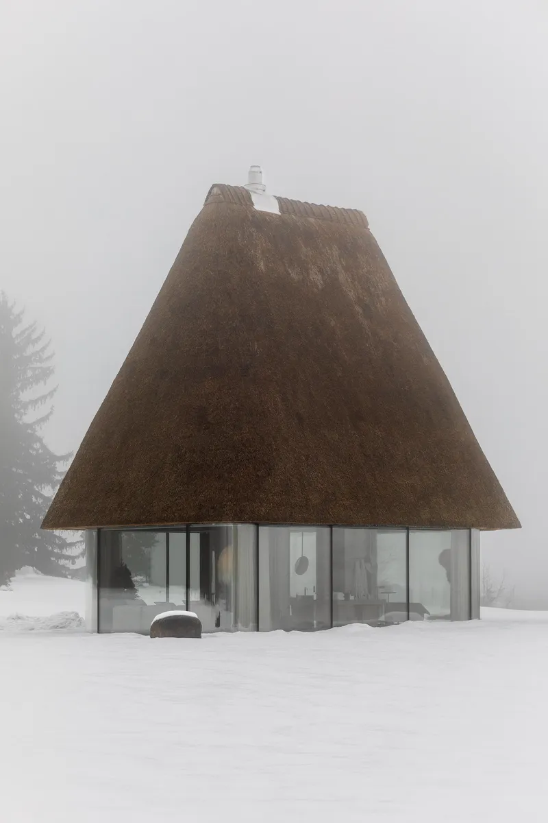 Thatched roof pavilion with glass walls surrounded by heavy snow and fog