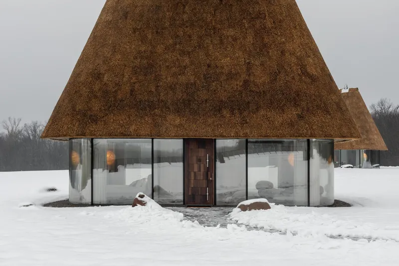 Front entrance with timber door and continuous glass facade beneath the sloping thatched roof