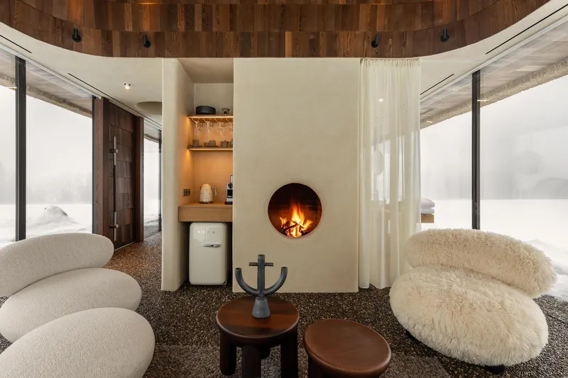Central fireplace wall with kitchenette niche flanked by floor-to-ceiling glazing overlooking snow