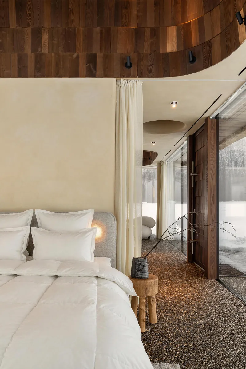 Bedroom with curved wood-paneled ceiling and full-height glazing overlooking a snowy landscape