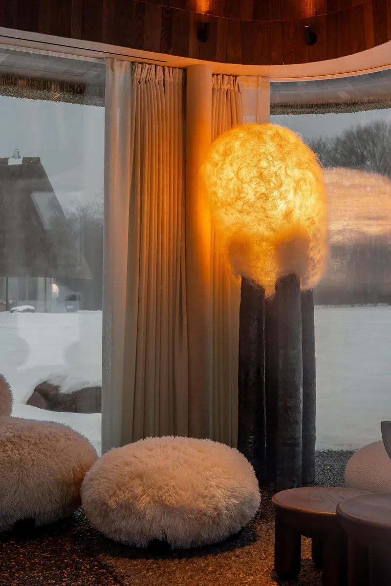 Spherical illuminated pendant on black pedestals beside floor cushions at dusk