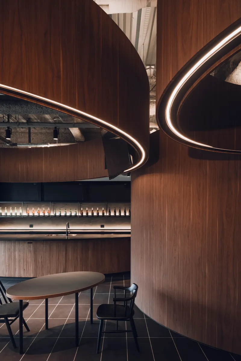 Close-up of overlapping curved timber walls with integrated LED ring lighting beneath exposed structural ceiling