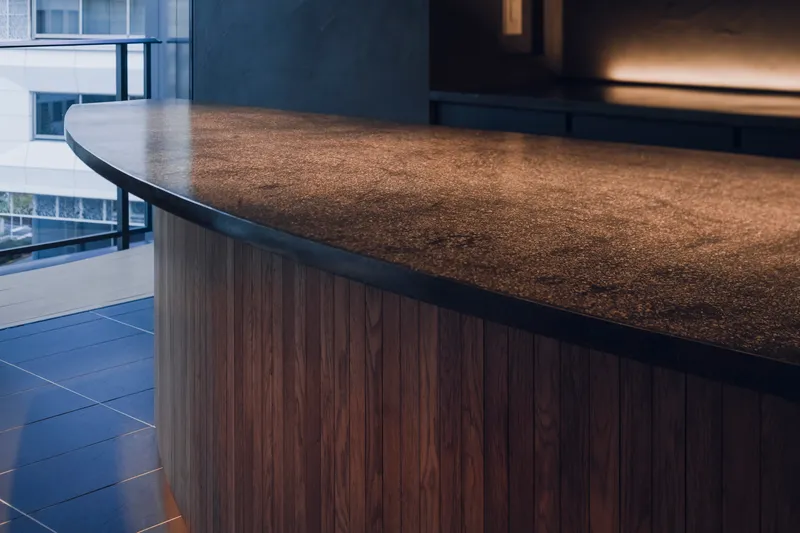 Close-up of the curved stone counter edge with walnut base cladding near a glazed opening