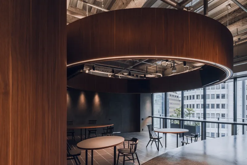 Spiraling wood canopy with mirrored underside reflecting exposed services and floor-to-ceiling windows overlooking adjacent buildings