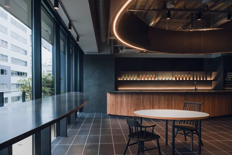 Office breakroom with floor-to-ceiling windows, walnut cabinetry, and circular LED light fixture above exposed mechanical ceiling