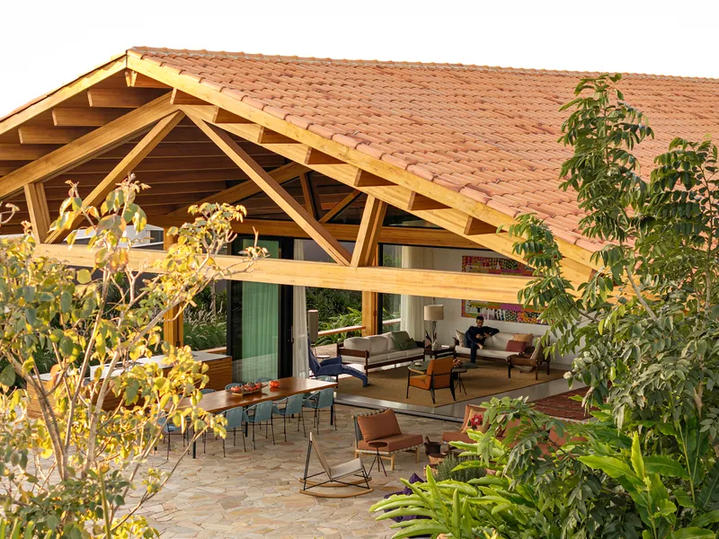 Open-air terrace under a clay tile roof with exposed timber trusses and tropical plantings