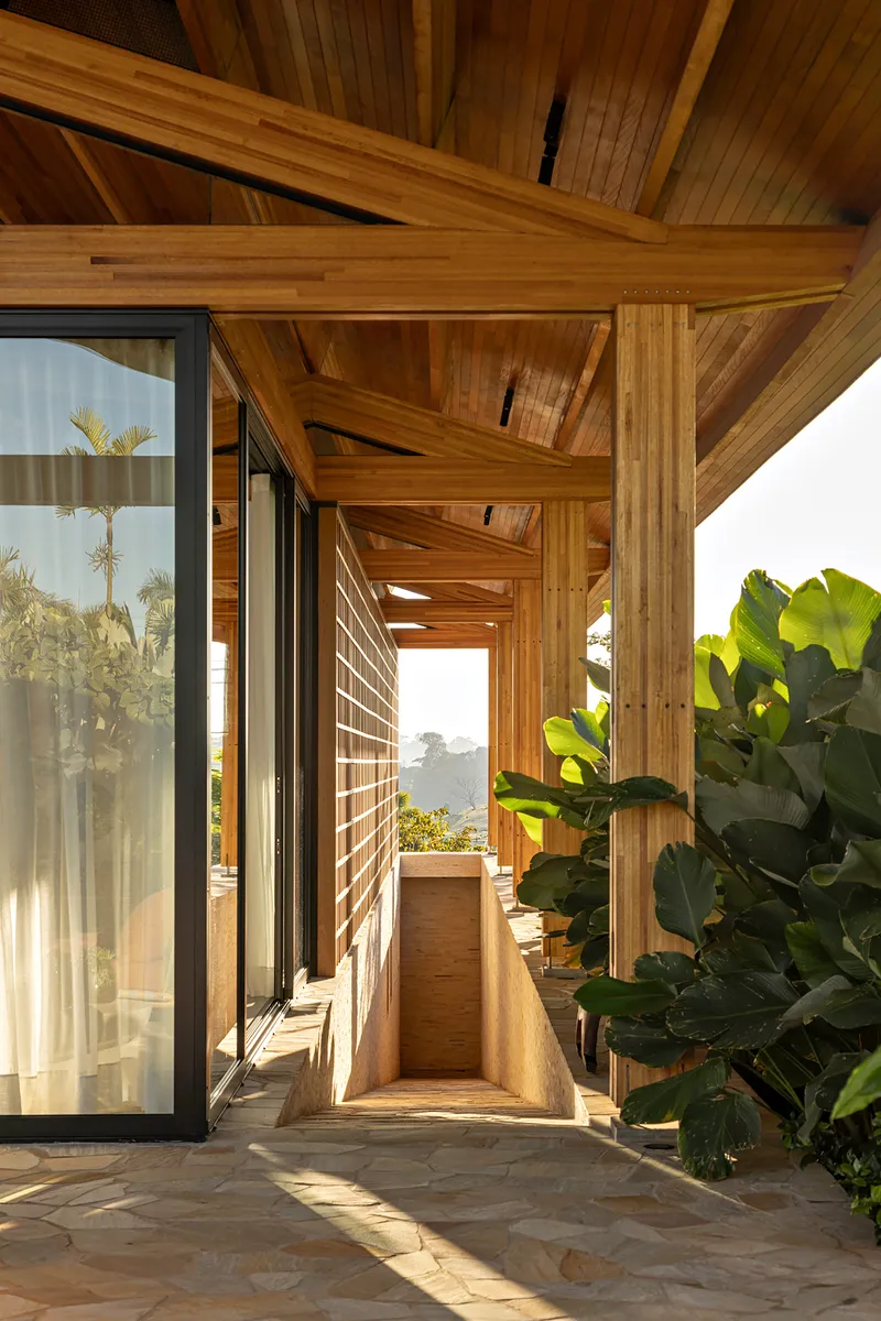 Covered walkway with timber columns and horizontal slatted screen framed by banana leaves