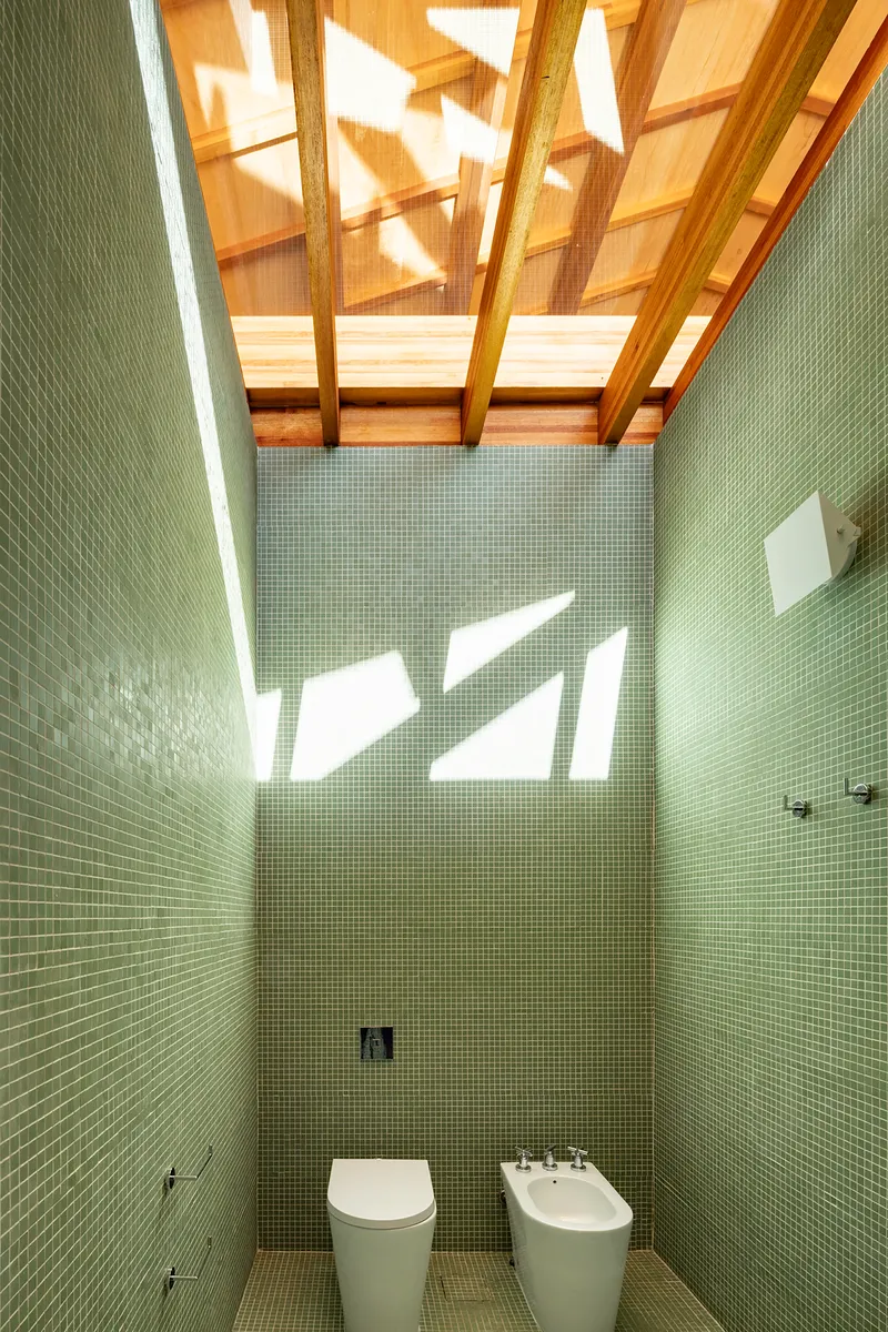 Bathroom clad in green mosaic tile with skylights casting geometric shadows overhead
