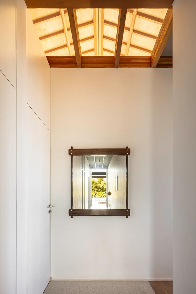 White-walled interior room with timber skylight above and dark-framed window opening framing garden view