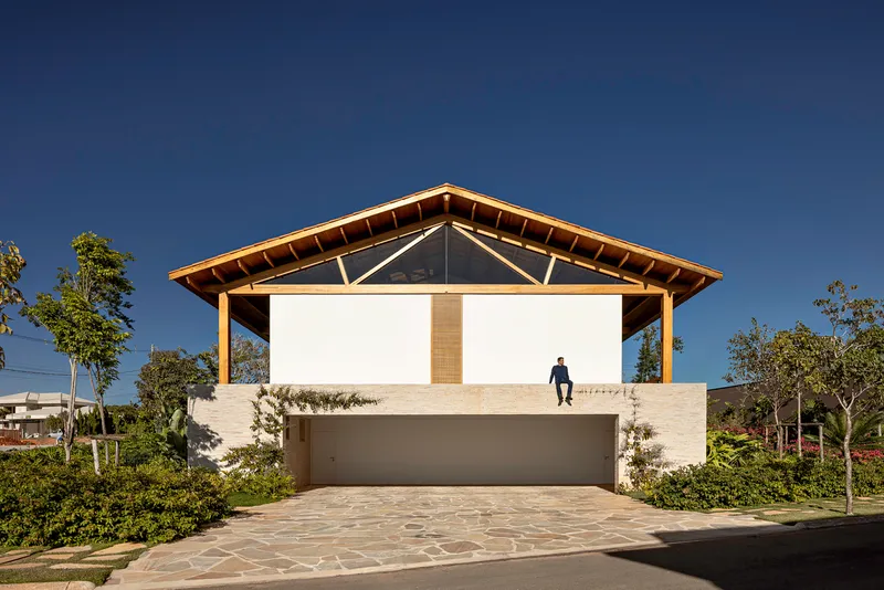 Street facade with exposed timber roof structure, white masonry base, and a figure standing on the upper terrace