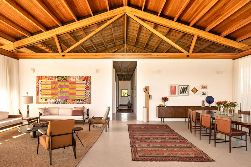 Open-plan living and dining space beneath exposed timber trusses and tongue-and-groove ceiling planks