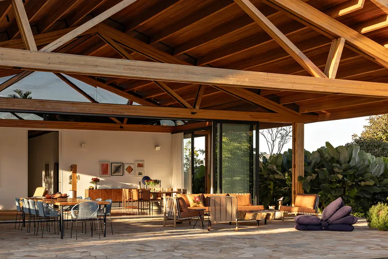 Covered outdoor terrace with stone paving and exposed timber trusses opening to lush tropical planting