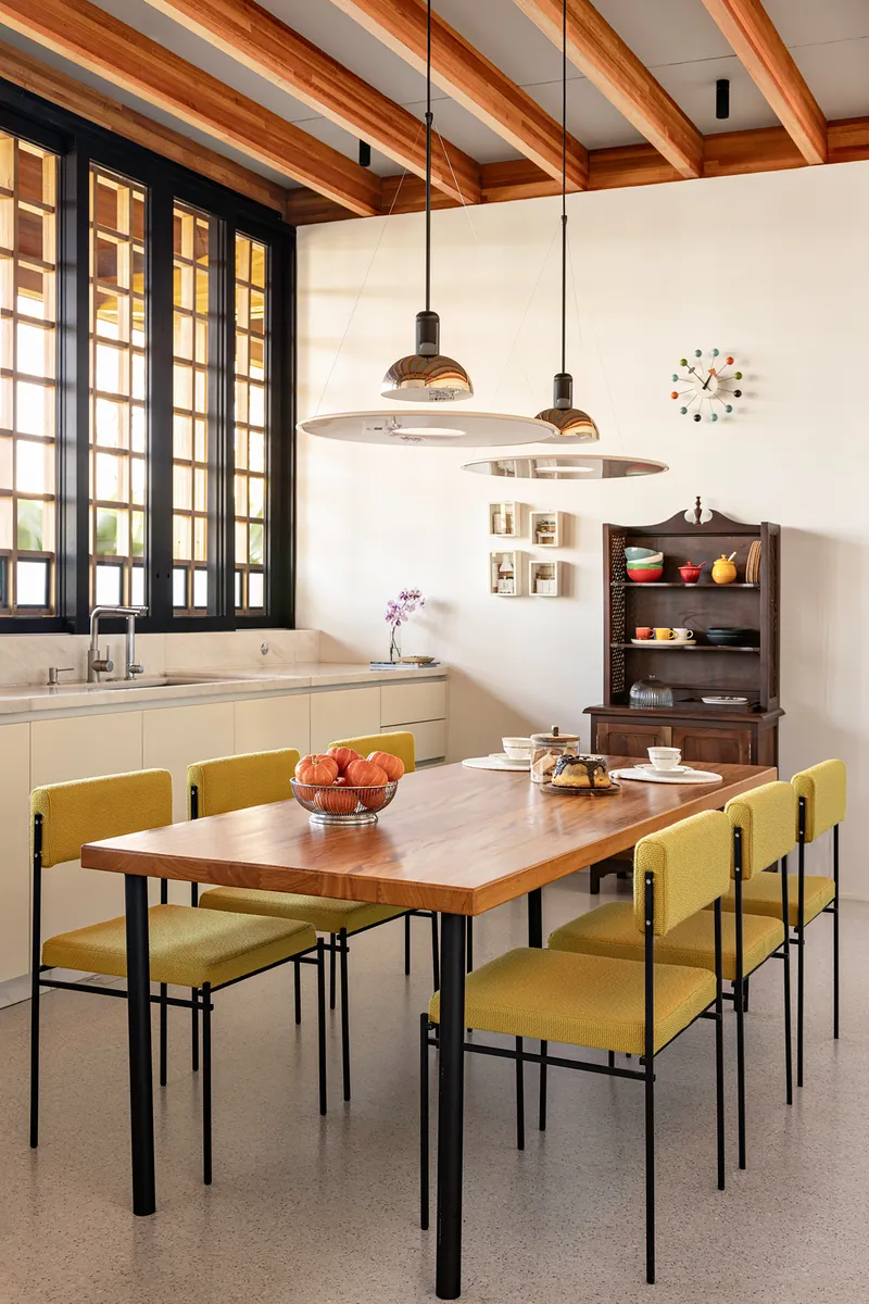 Dining area with timber table, olive upholstered chairs and dark gridded windows under exposed beam ceiling