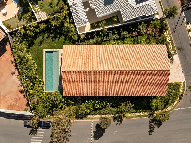 Aerial view of tiled roof volume beside rectangular pool surrounded by mature trees and garden plantings