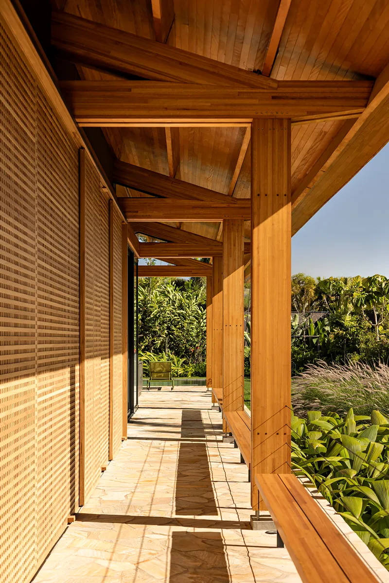 Covered timber walkway with woven screen wall casting dappled shadows on sandstone pavers at midday