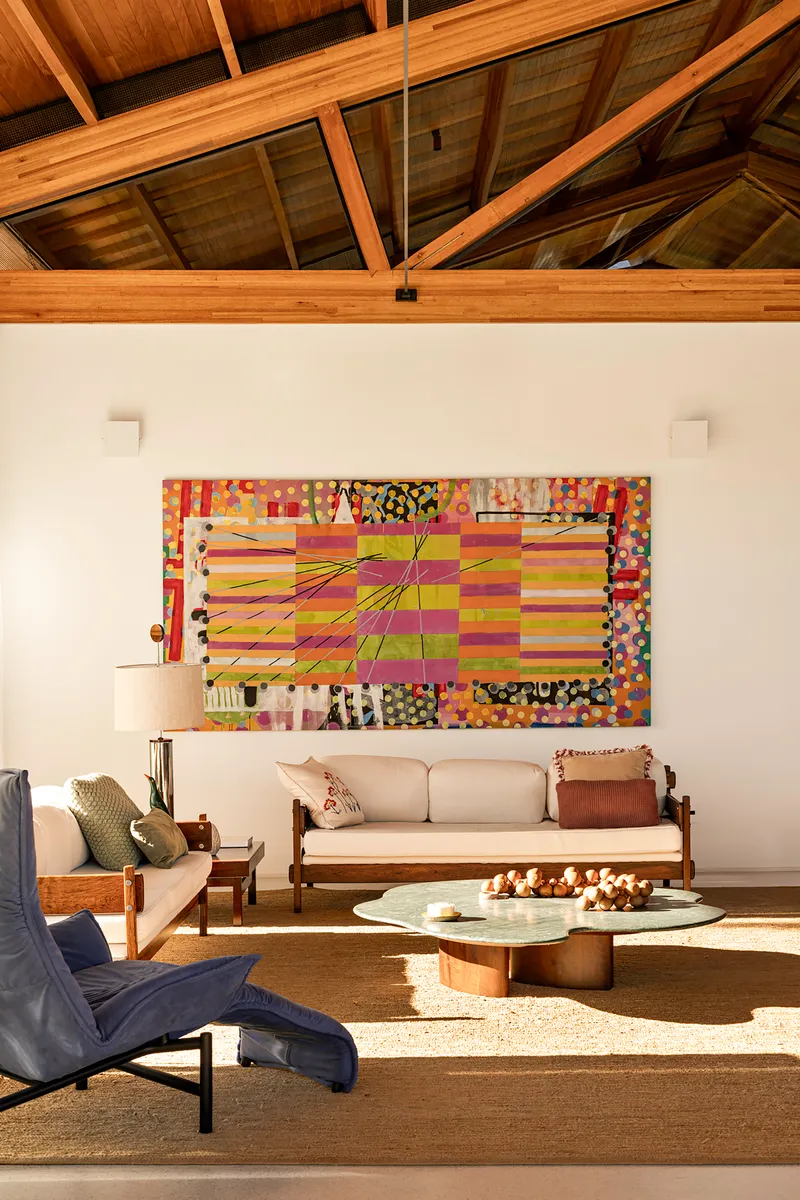 Living room with exposed timber truss ceiling and abstract artwork above a low sofa in afternoon light