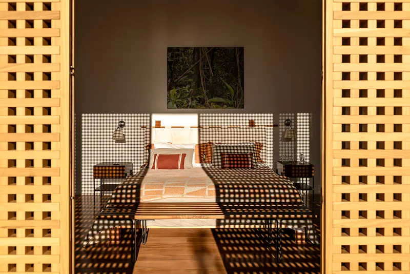 Bedroom framed by yellow perforated brick walls with chequered screens creating dappled shadows across the interior
