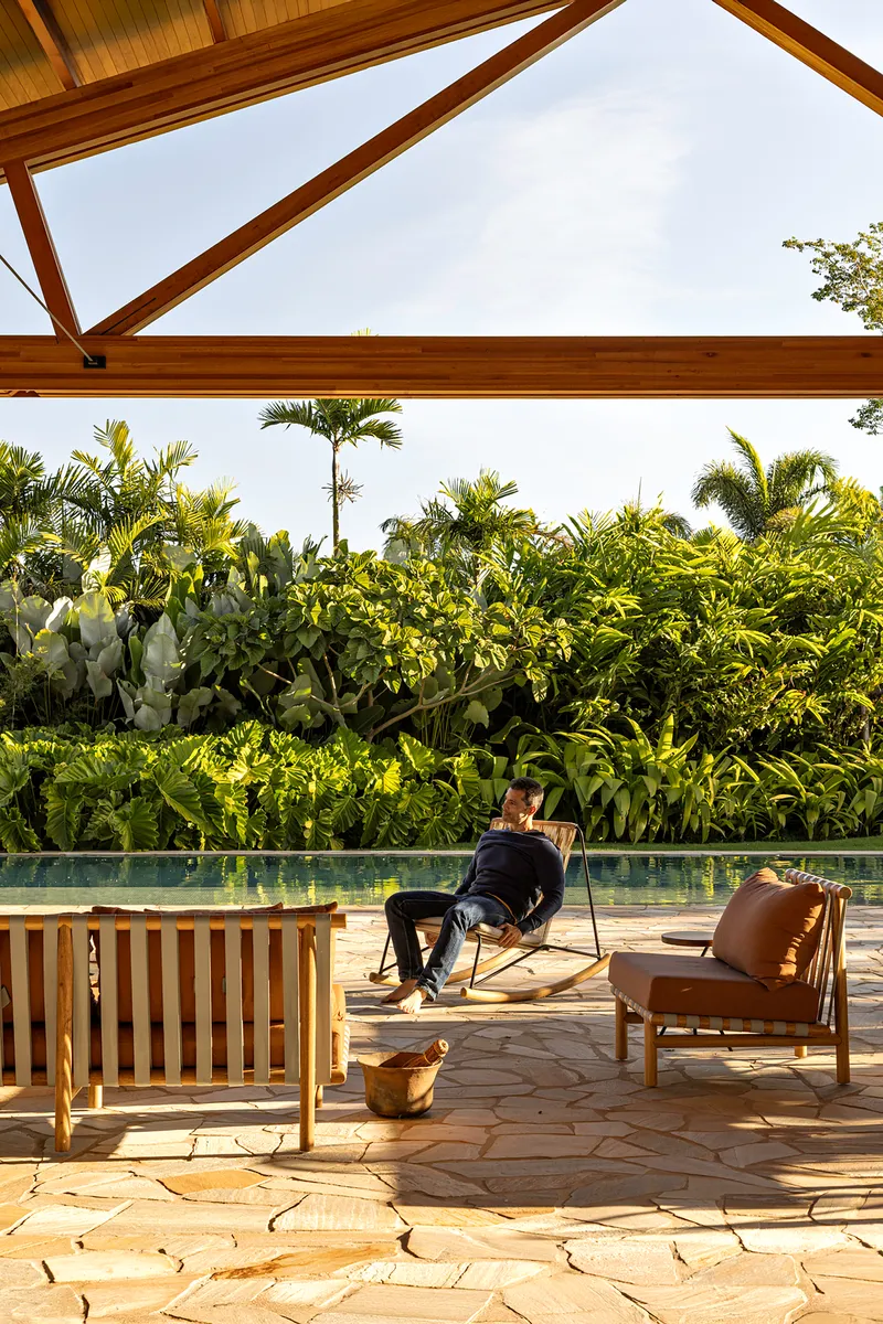 Covered terrace with stone paving and timber benches beside a pool backed by dense tropical planting
