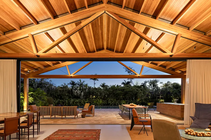 Exposed timber truss ceiling above the open living area looking out to the garden at dusk