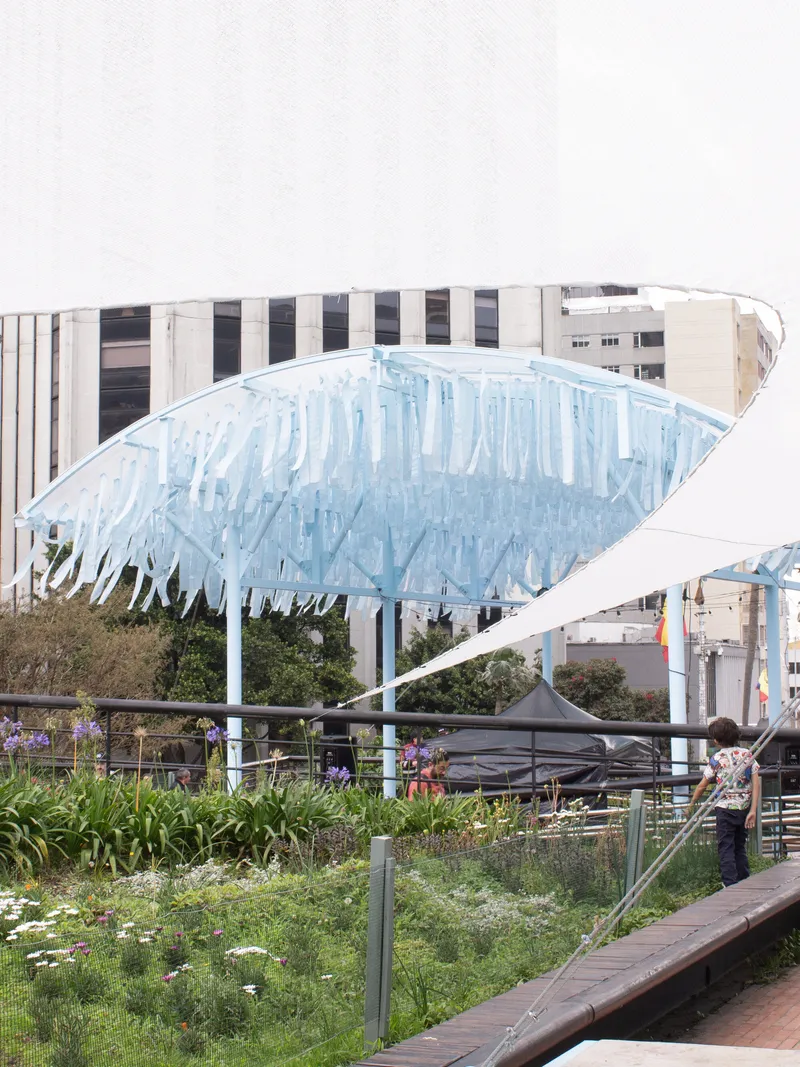 Close view of one curved canopy with vertical blue fins above a planted garden bed and visitor