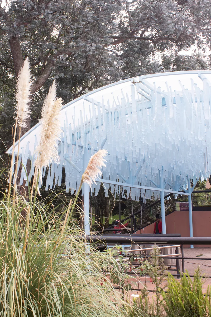 Edge of the vaulted canopy with hanging translucent strips above ornamental grasses and pampas plumes